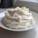 A swirl of fluffy, white cream cheese frosting piled high in a small white bowl.