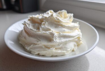 A swirl of fluffy, white cream cheese frosting piled high in a small white bowl.