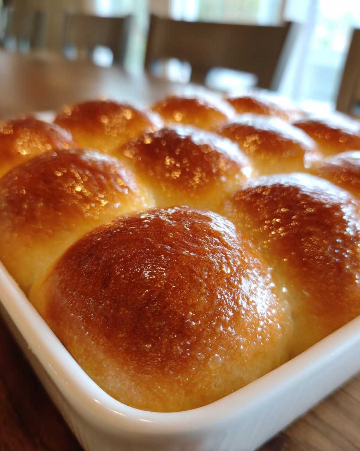 Close-up of golden brown, shiny, fluffy dinner rolls baked together in a white square dish.