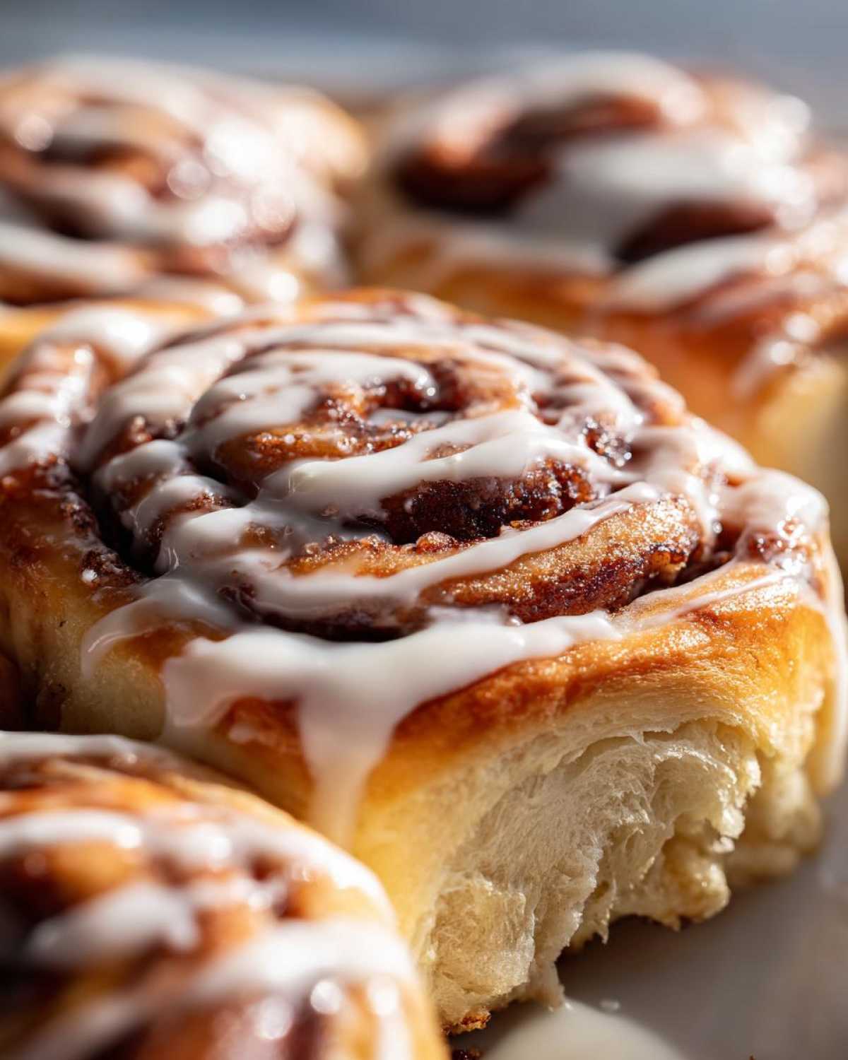 Extreme close-up of a freshly baked cinnamon roll topped with white icing, showing the soft, fluffy interior dough.