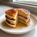 A tall stack of fluffy greek yogurt pancakes drizzled with maple syrup on a white plate.