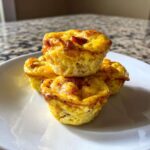 Three fluffy muffin tin egg bites stacked on a white plate, showing golden-brown tops.