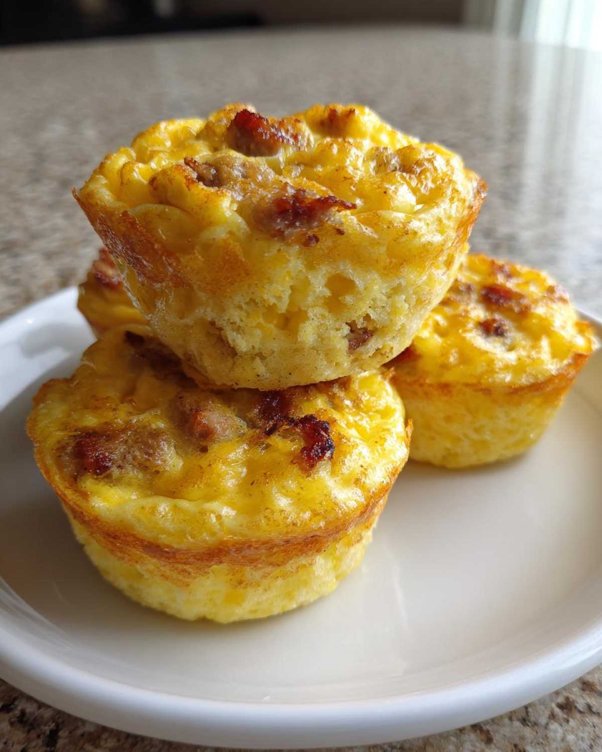 A stack of four fluffy muffin tin egg bites, featuring visible chunks of sausage, served on a white plate.