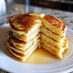 A tall stack of incredibly fluffy pancakes, cut to show the airy interior, topped with melting butter and syrup.