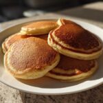 A close-up of a stack of golden brown sourdough pancakes piled high on a white plate.