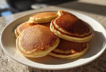 A close-up of a stack of golden brown sourdough pancakes piled high on a white plate.