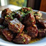 A white bowl filled with tender, cubed crockpot steak bites coated in a glistening garlic and herb sauce.