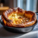 A golden brown, perfectly risen yorkshire pudding baked in a small black cast iron skillet.