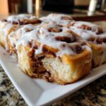 A close-up view of several gooey, frosted cinnamon rolls, with one roll showing a bite taken out, revealing the soft interior.