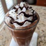 Close-up of a glass filled with rich frozen hot chocolate topped with whipped cream, chocolate syrup, and shavings.