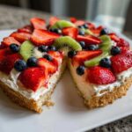 Close-up of a fruit pizza sugar cookie with cream cheese frosting topped with strawberries, kiwi, and blueberries.