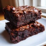 Two stacked, fudgy black bean brownies topped with melted chocolate chips on a white plate.