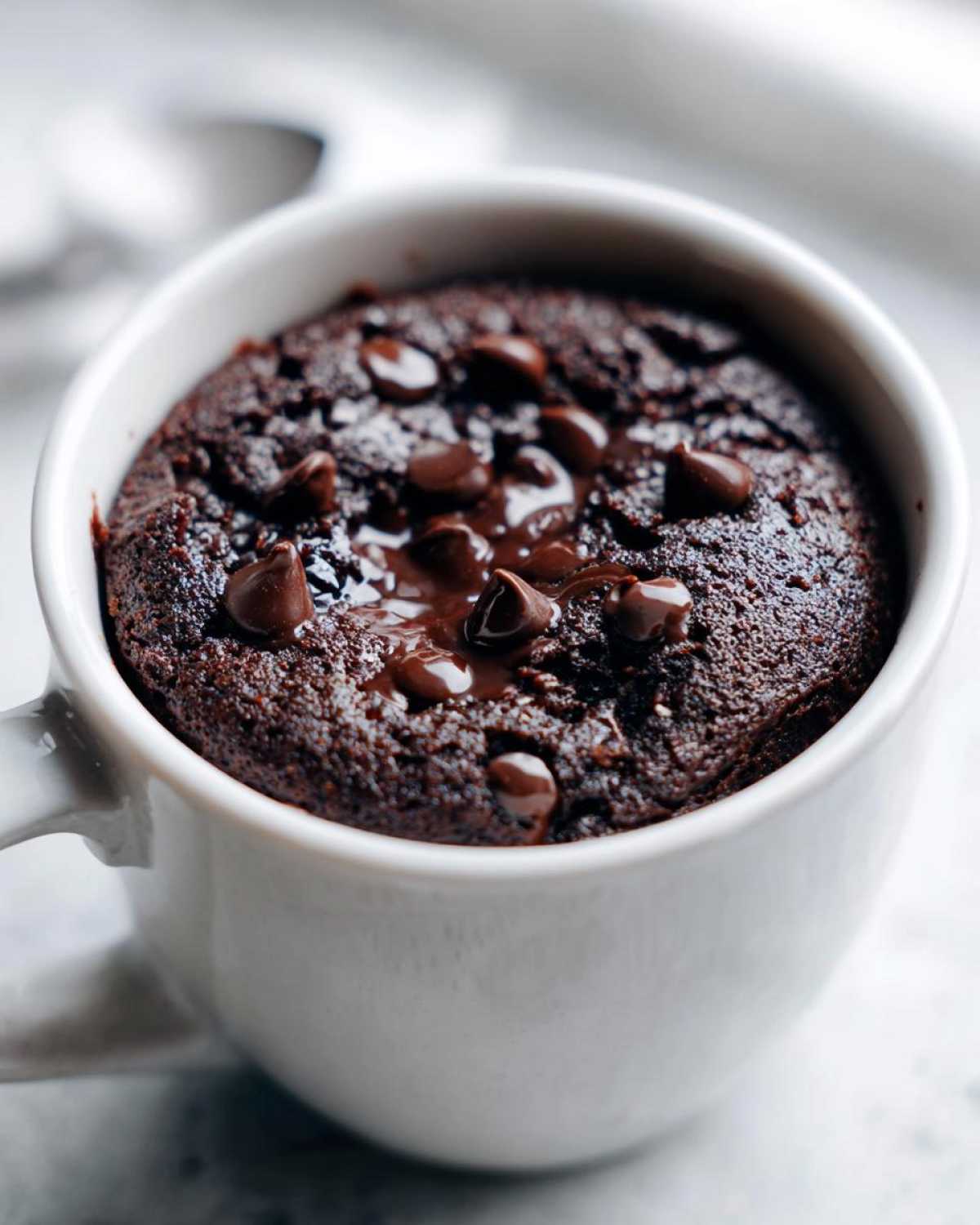 Close-up of a rich, dark chocolate mug cake topped with melted chocolate chips.