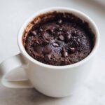 Close-up of a fudgy chocolate mug cake topped with melted chocolate chips inside a white mug.