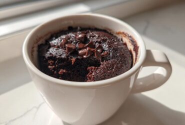 Close-up of a rich, fudgy chocolate mug cake topped with melted chocolate chips, sitting in a white mug.