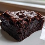 Close-up of a rich, fudgy slice of sweet potato brownies topped with melted chocolate chips on a white plate.