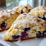 Close-up of freshly baked blueberry scones topped with a sweet white glaze on a white plate.
