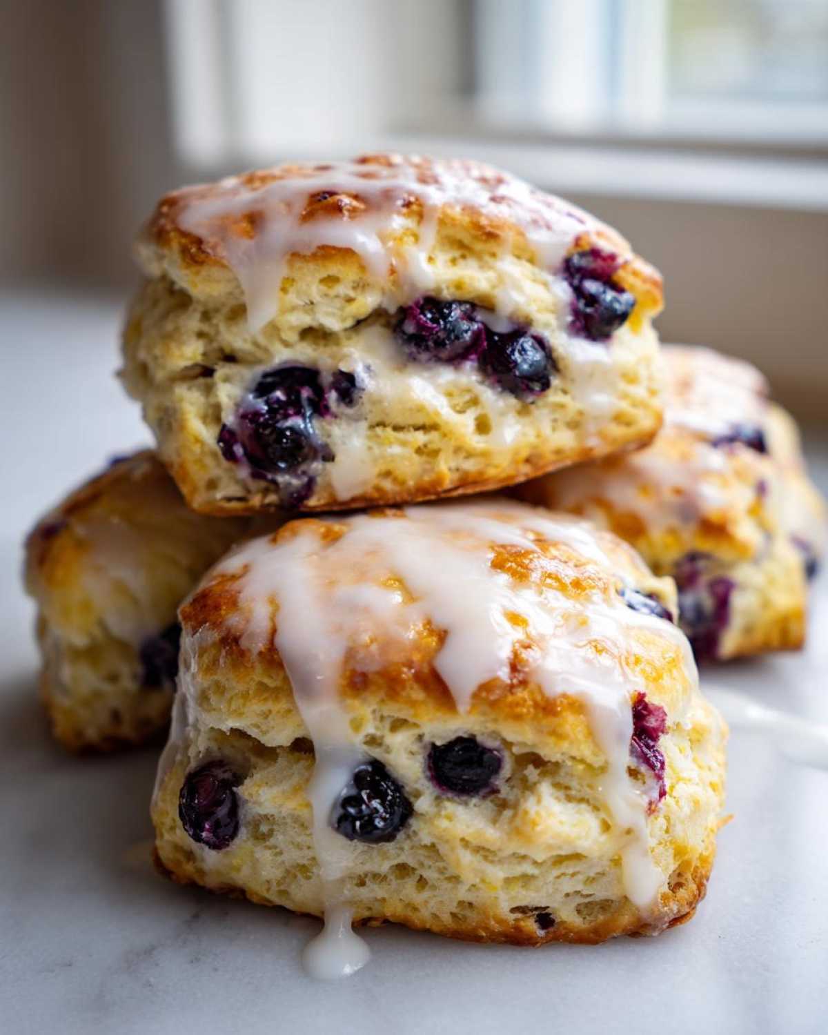 Close-up of stacked, freshly baked blueberry scones topped with a thick, dripping vanilla glaze.