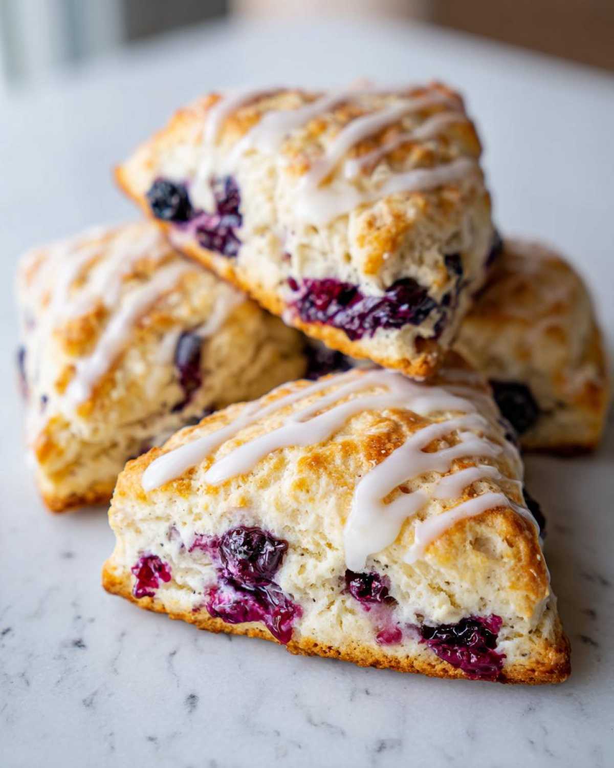 Close-up of several freshly baked blueberry scones drizzled with white icing, featuring visible blueberries.