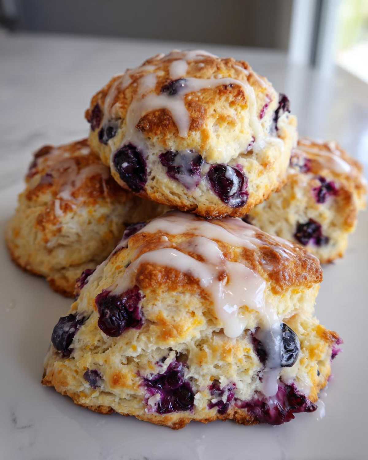 Close-up of a stack of four golden brown blueberry scones drizzled with white vanilla glaze.