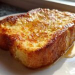 Close-up of a thick, golden brown slice of easy french toast glistening with syrup on a white plate.
