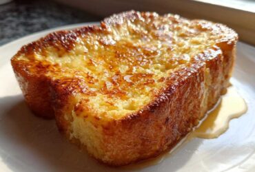 Close-up of a thick, golden brown slice of easy french toast glistening with syrup on a white plate.
