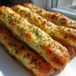 A close-up stack of golden, buttery garlic breadsticks topped with fresh parsley, ready to eat.