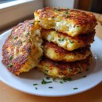 A stack of four golden brown, pan-fried mashed potato cakes garnished with fresh chives.