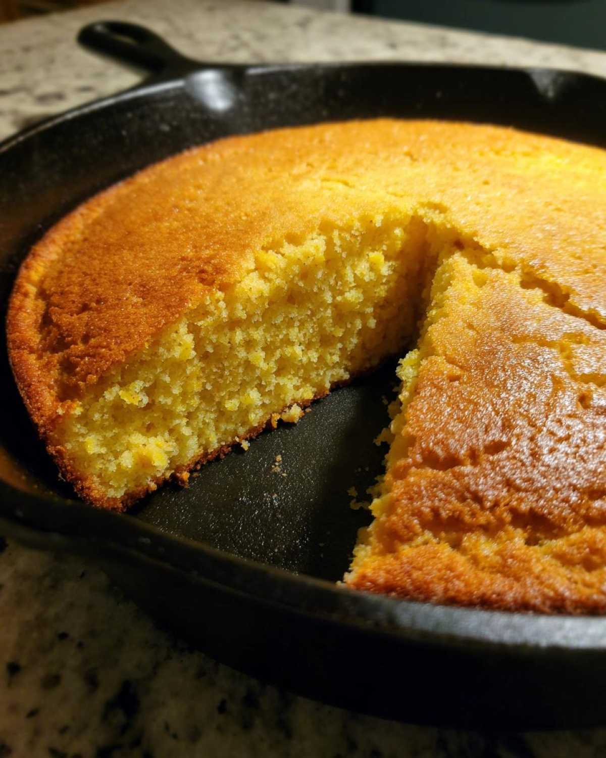 Close-up of golden brown skillet cornbread in a cast iron pan with one slice cut out.