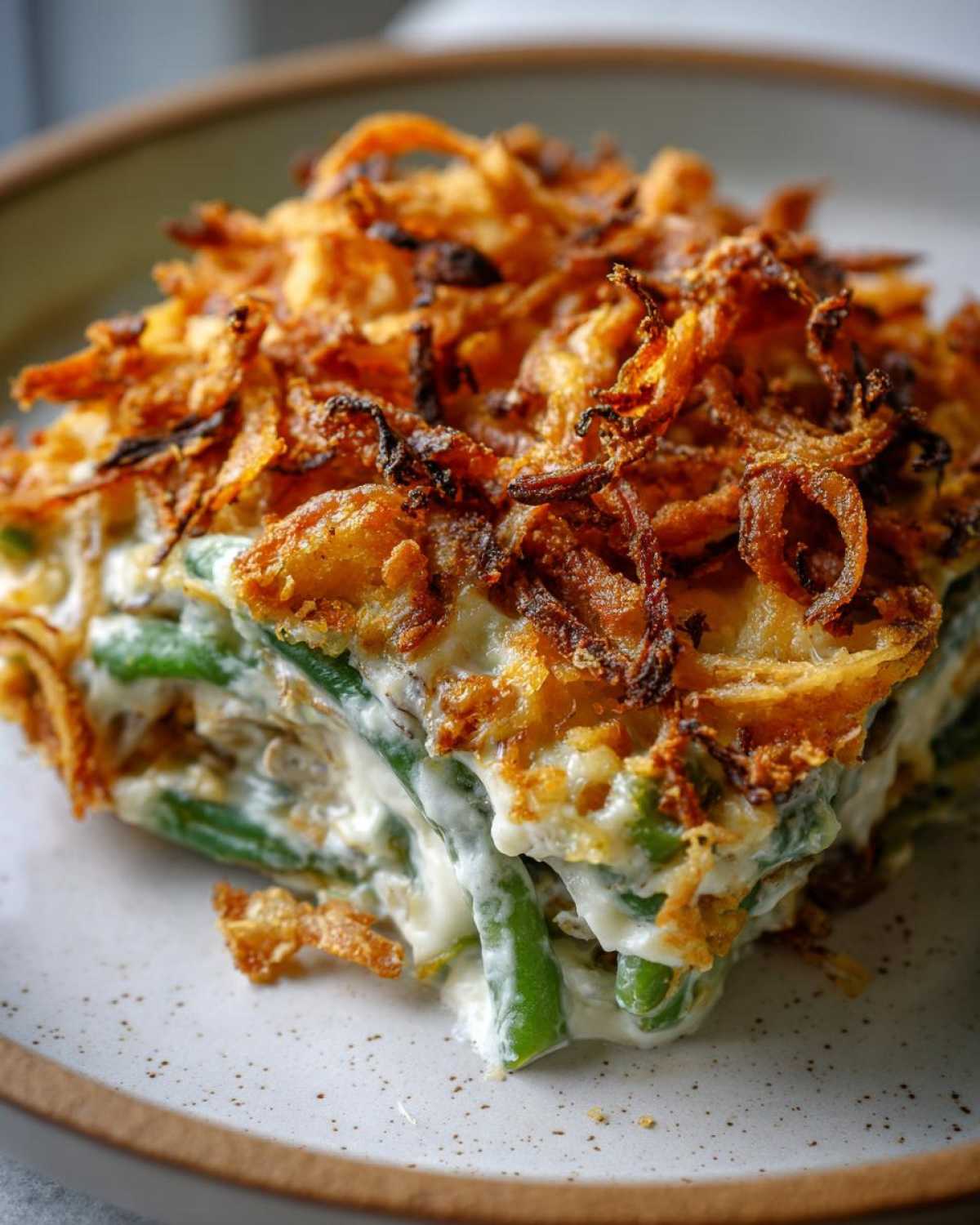 Close-up of a square serving of creamy green bean casserole topped with golden, crispy fried onions.