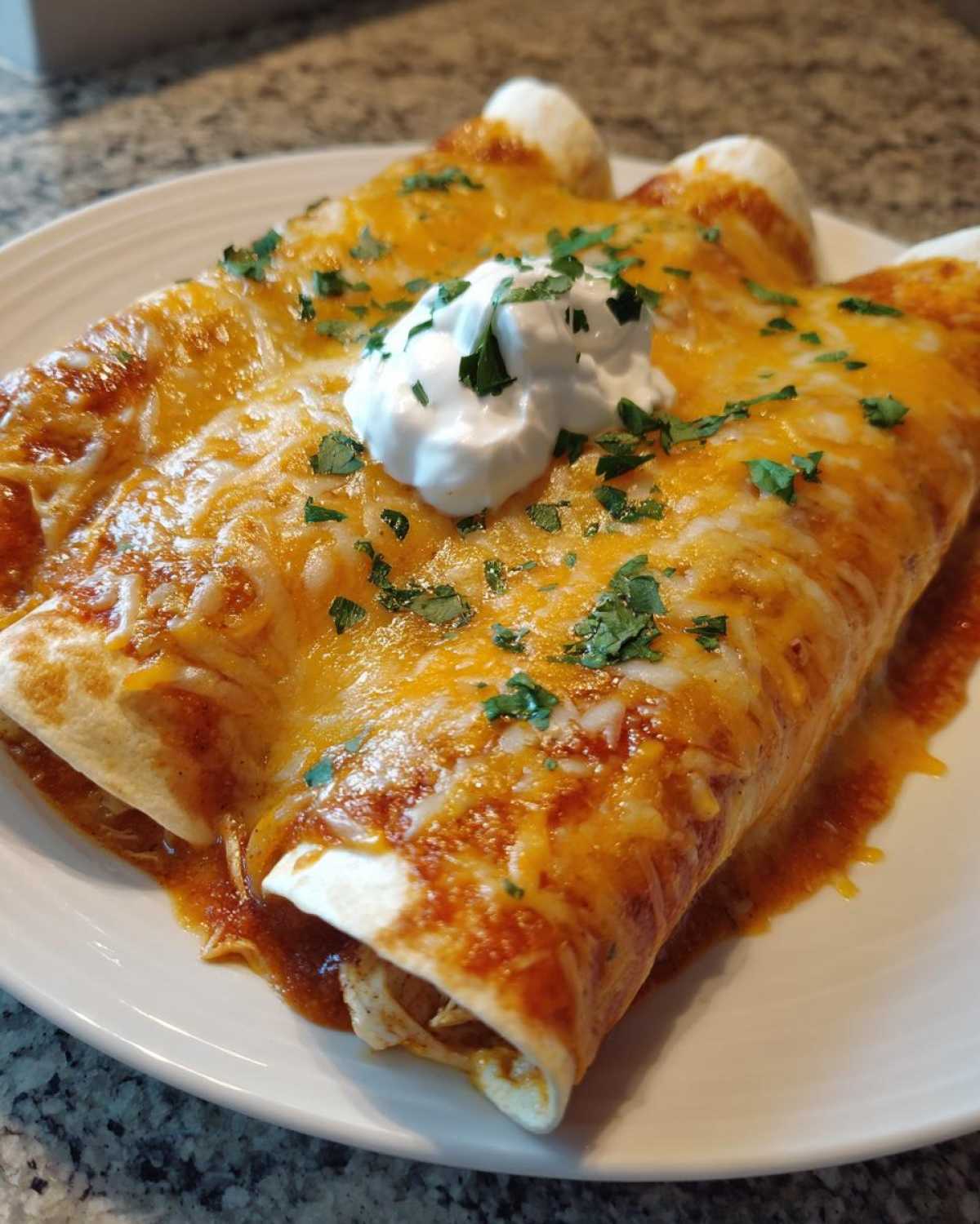 Two rolled green chile chicken enchiladas covered in melted orange cheese and sour cream.