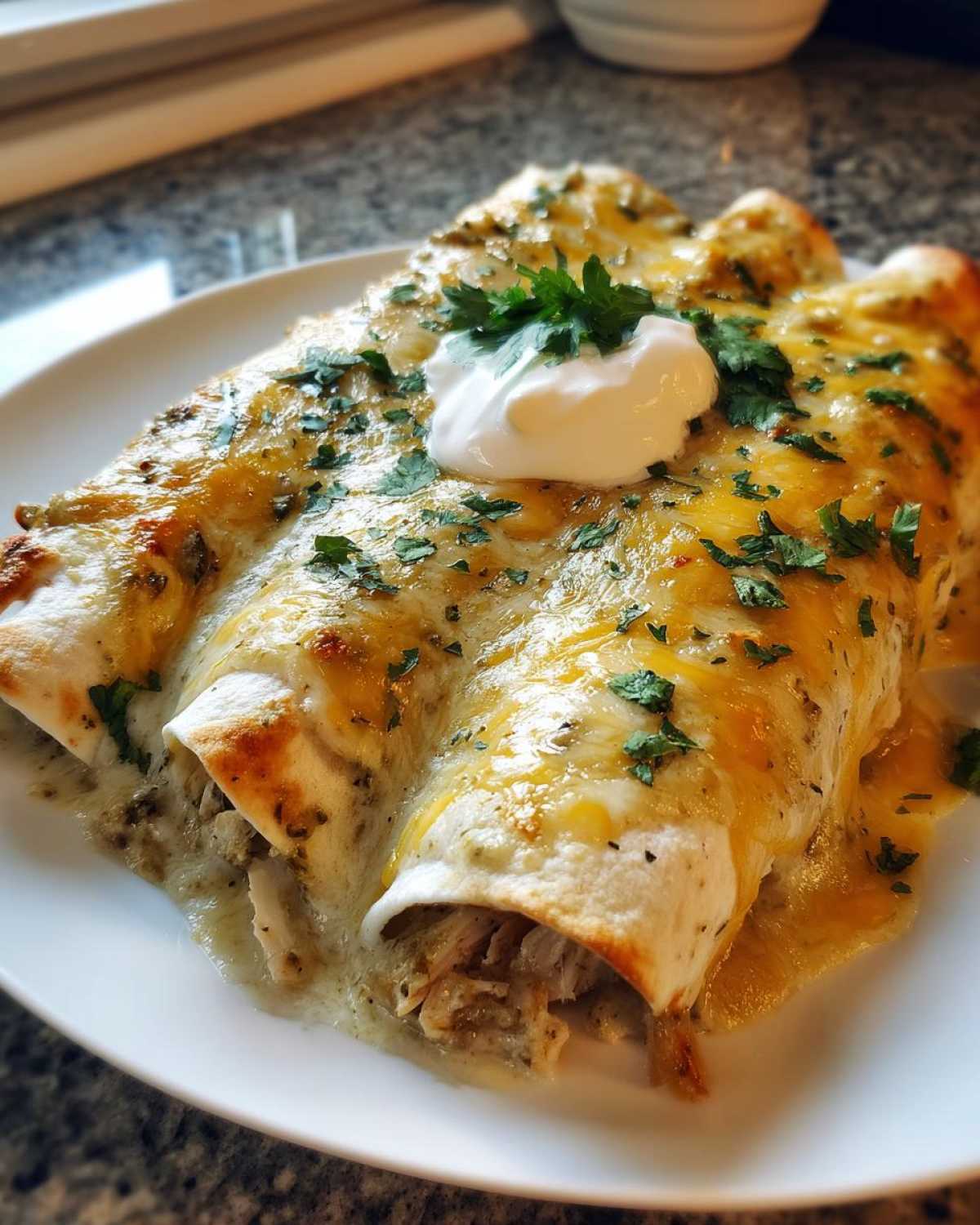 Three delicious green chile chicken enchiladas covered in melted cheese, sour cream, and cilantro.
