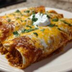 Close-up of two baked green chile chicken enchiladas covered in melted cheese, sauce, and sour cream.