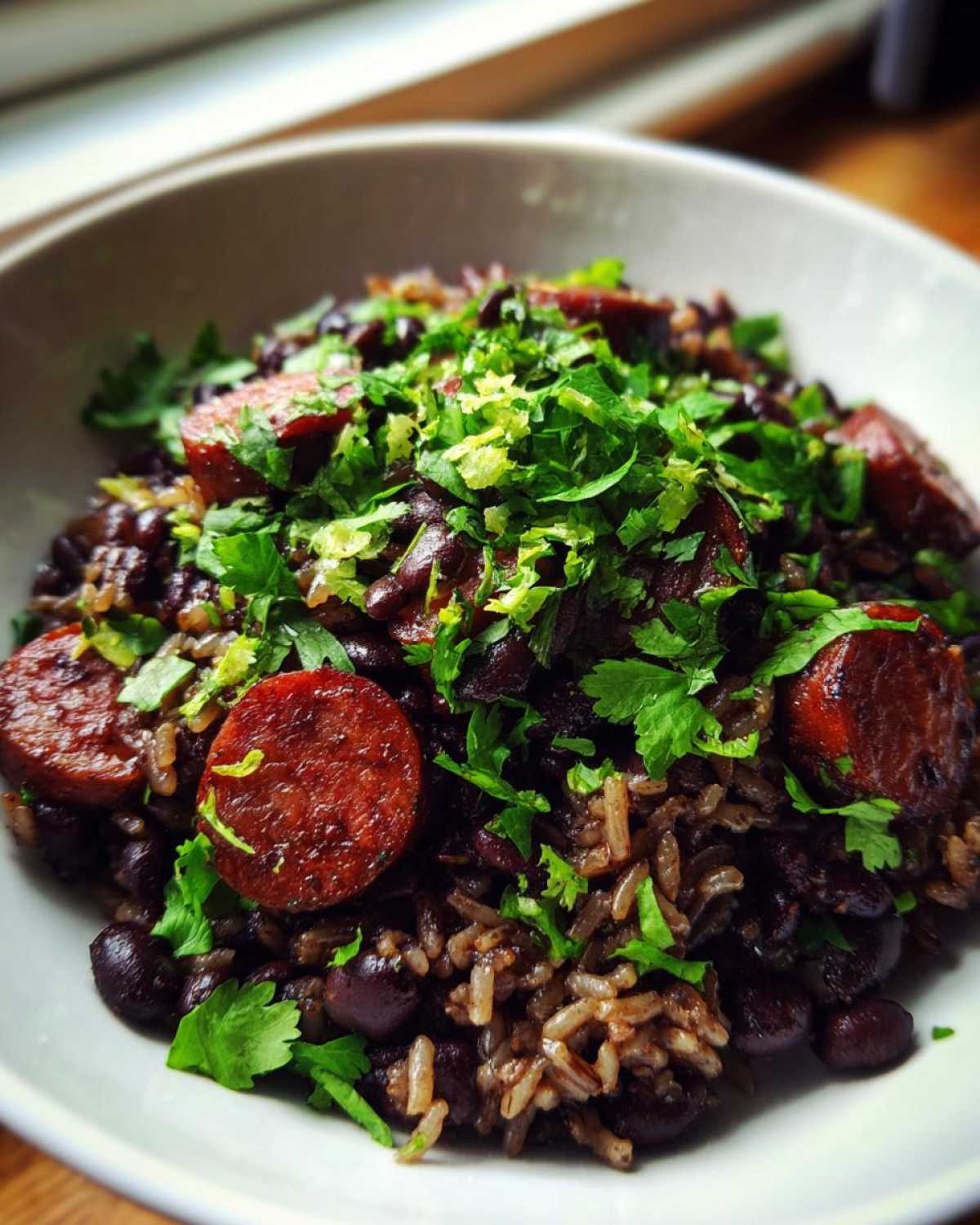 Close-up of a bowl of hearty black beans and rice mixed with sliced sausage and topped with fresh cilantro.