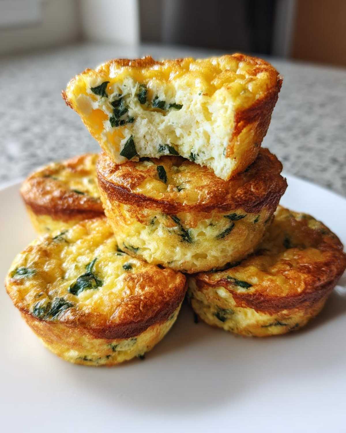 A stack of golden-brown, high-protein egg bites, with the top one broken open to show the fluffy interior and spinach.