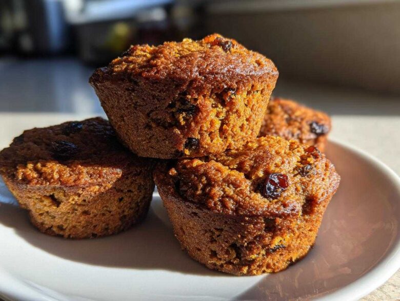 A close-up stack of four golden brown honey bran muffins dotted with raisins, sitting on a white plate.