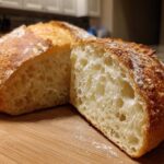 Close-up of a freshly baked Italian bread loaf cut in half, showing an open, airy crumb structure and golden crust.