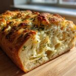 Close-up of a freshly baked Italian herb and cheese bread loaf cut open, showing soft interior and cheesy topping.