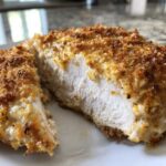 Close-up of juicy caesar chicken breast cut in half, showing white meat and a golden, crispy topping.