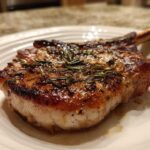 A thick, bone-in pork chop, perfectly seared and topped with rosemary, showing the results of the marinade for pork chops.