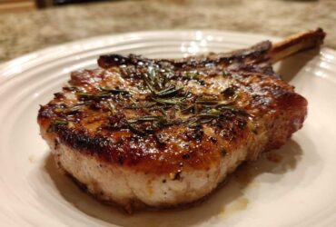 A thick, bone-in pork chop, perfectly seared and topped with rosemary, showing the results of the marinade for pork chops.