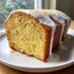 Close-up of a moist slice of lemon pound cake topped with dripping white glaze and zest.