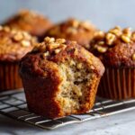 Close-up of a moist banana nut muffins with a bite taken out, showing the crumb texture and walnuts on top.