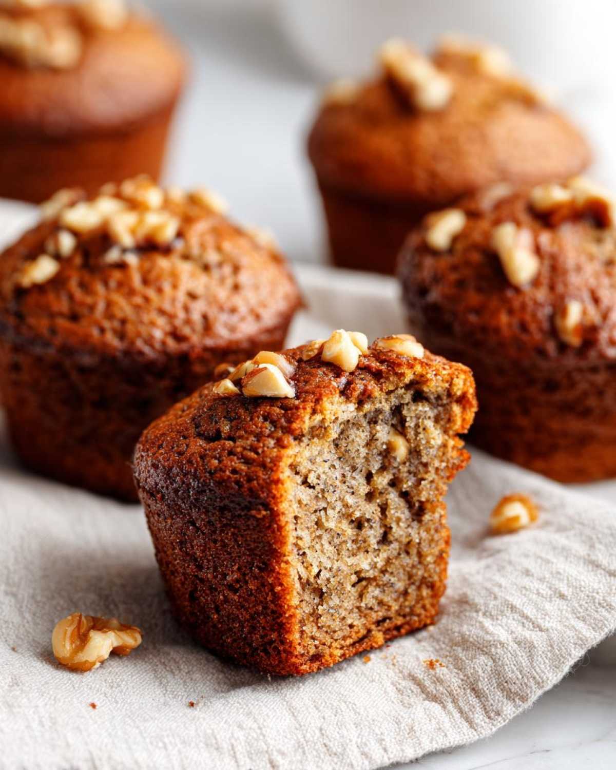 A close-up of a banana nut muffin with a bite taken out, revealing the moist interior and topped with walnuts.