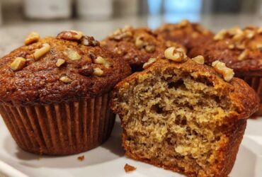Close-up of moist banana nut muffins, one cut open showing the texture, topped with walnuts.