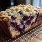 A loaf of moist blueberry banana bread featuring a crumb topping and bursting with blueberries.