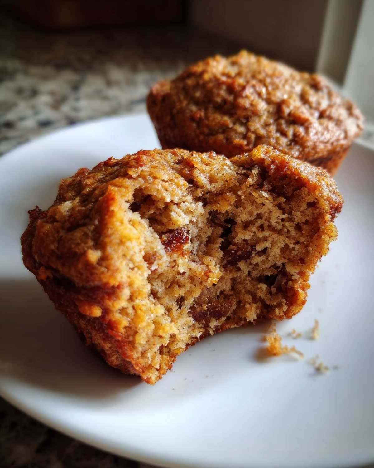Close-up of a bitten bran muffin showing the moist interior texture and raisins, with another muffin in the background.