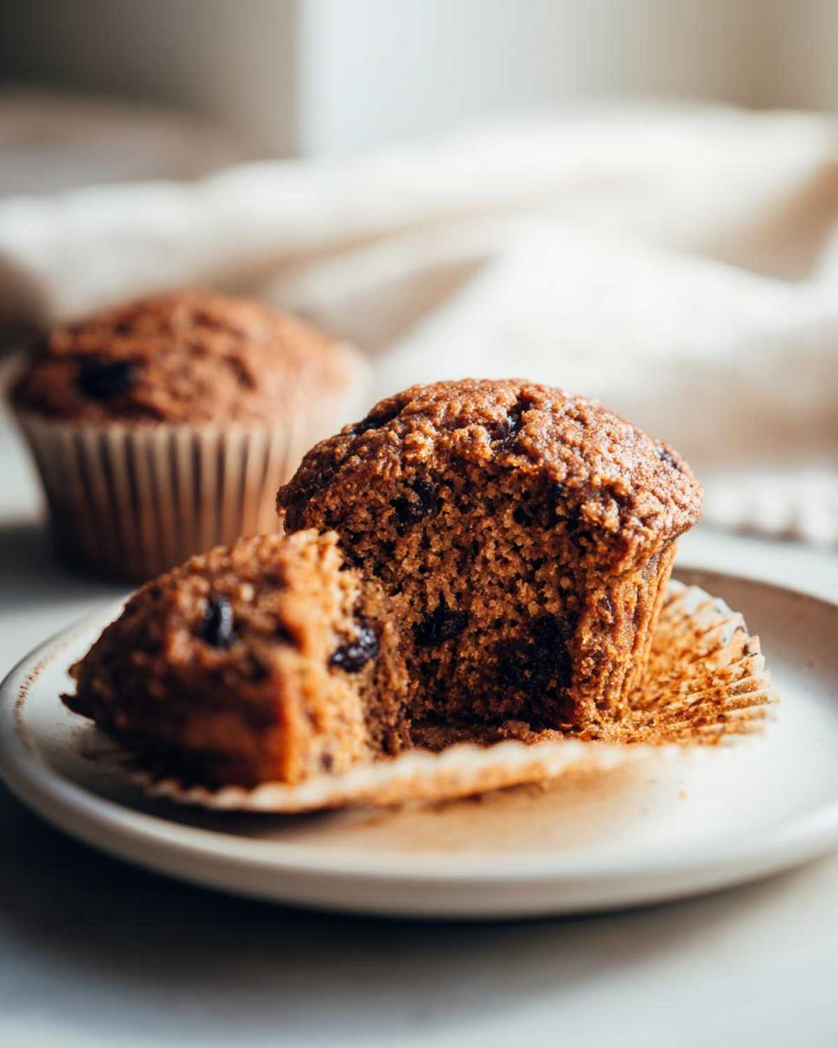 A bran muffin broken in half on a plate, showing its moist texture and dark raisins. Perfect for low-calorie bran muffins.