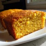 Close-up of a golden, moist slice of buttermilk cornbread showing its crumb texture on a white plate.