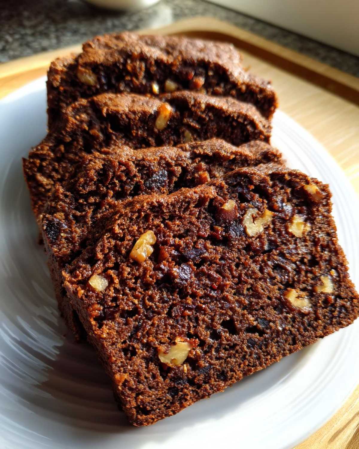 Close-up of several moist slices of dark brown date nut bread studded with walnuts on a white plate.
